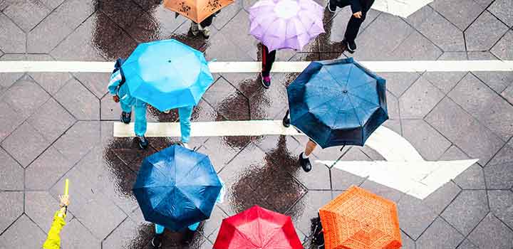 Image from above of people navigating a busy street under colourful umbrellas on a wet day